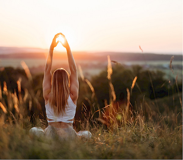 Woman doing yoga in a field at sunset