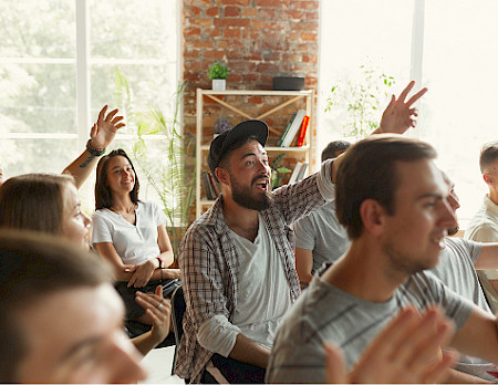 A group of people in an indoor workshop with their hands raised to ask questions.