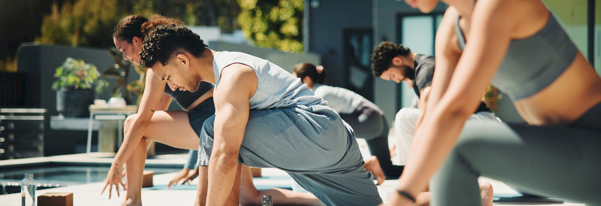 A group of people practicing a low-lunge yoga pose together on a bright outdoor terrace.