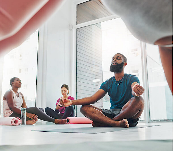 A man meditating in a seated pose on a yoga mat within a bright, modern studio.