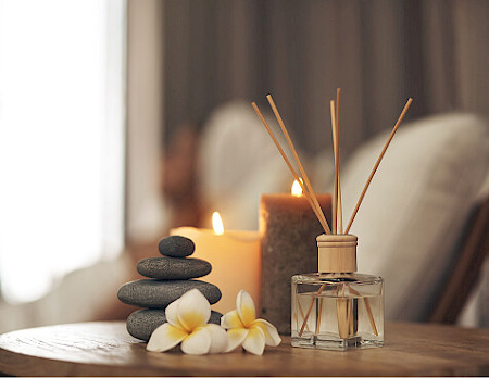 A peaceful wellness setup featuring an essential oil reed diffuser, lit candles, and stacked Zen stones on a wooden table.