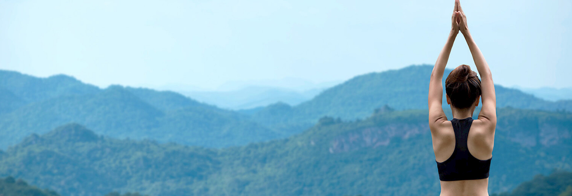 Silhouette of a person practicing a tree pose on a mountain peak during a vibrant sunset.
