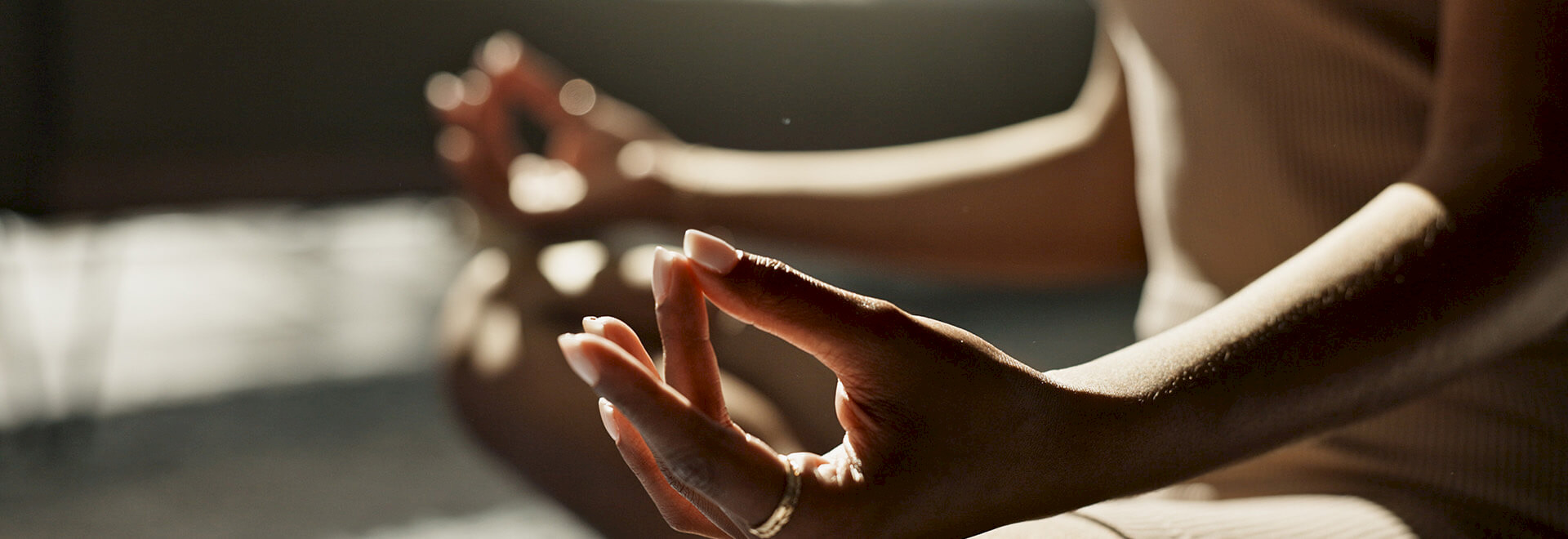 Close-up of a person's hands in a Gyan mudra meditation pose during a sunlit session.